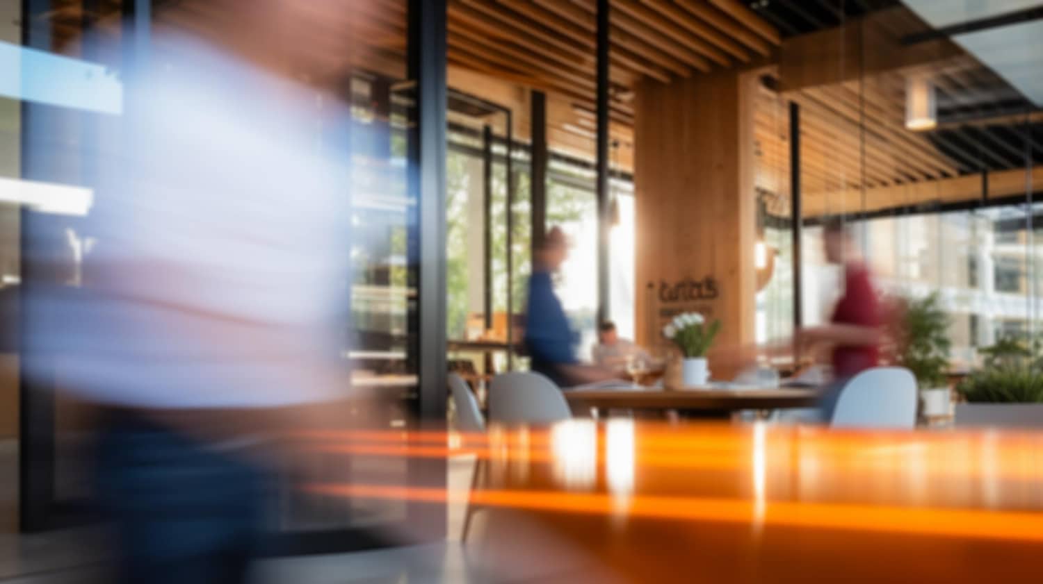 Blurred modern coworking space with people at tables and orange light streaks from moving lights.